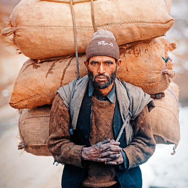 Portrait of a man carrying heavy load on his back in Anantnag, Jammu and Kashmir, India